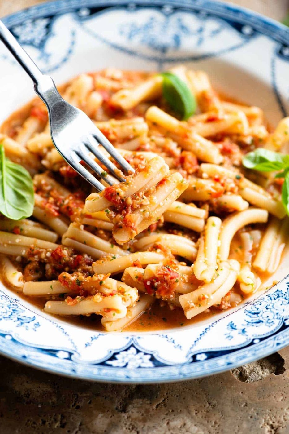A close up of a fork holing some pasta with a fresh tomato sauce in a blue and white bowl.