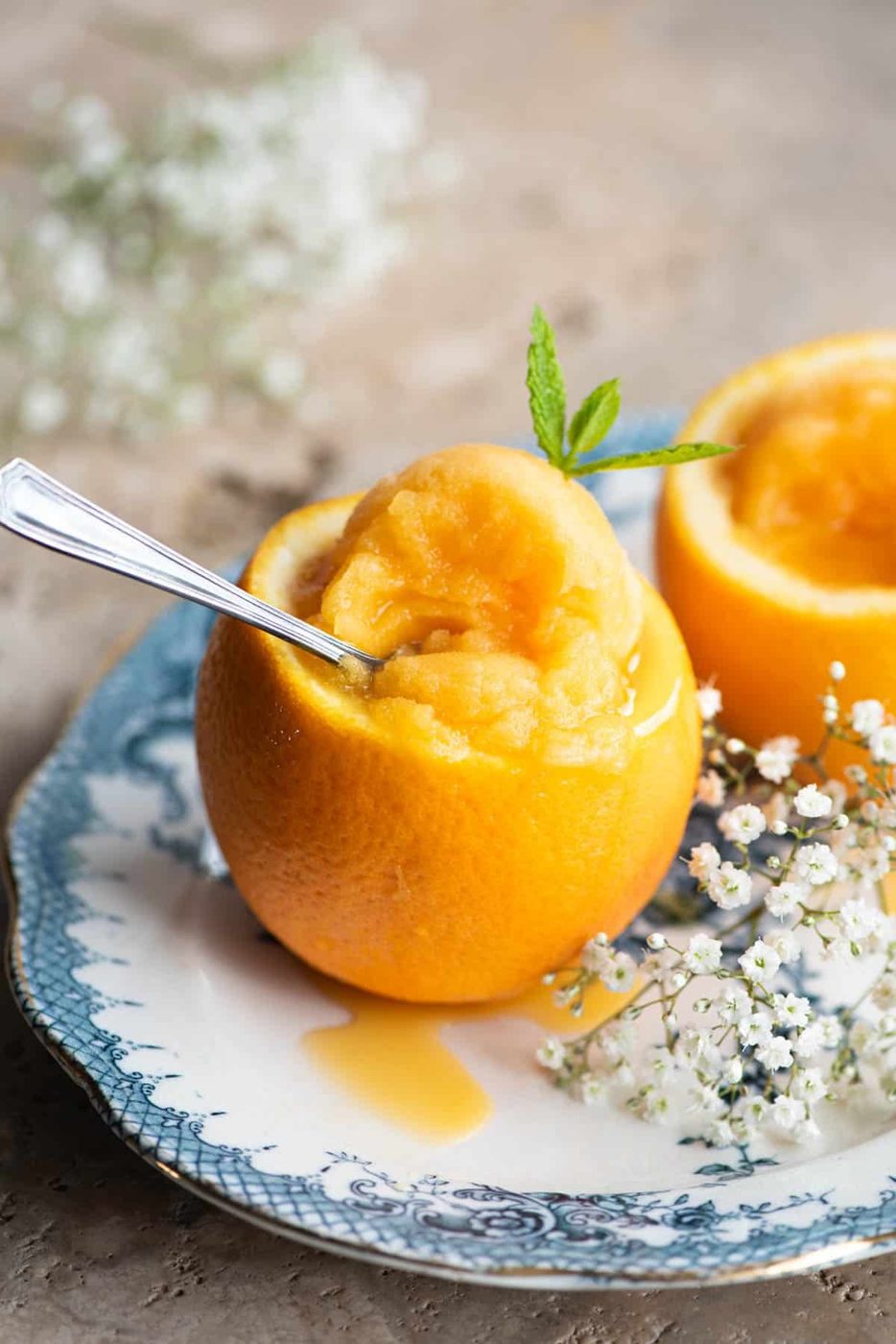 A close up of orange sorbet served inside an orange sitting on a blue plate with flowers at the side.