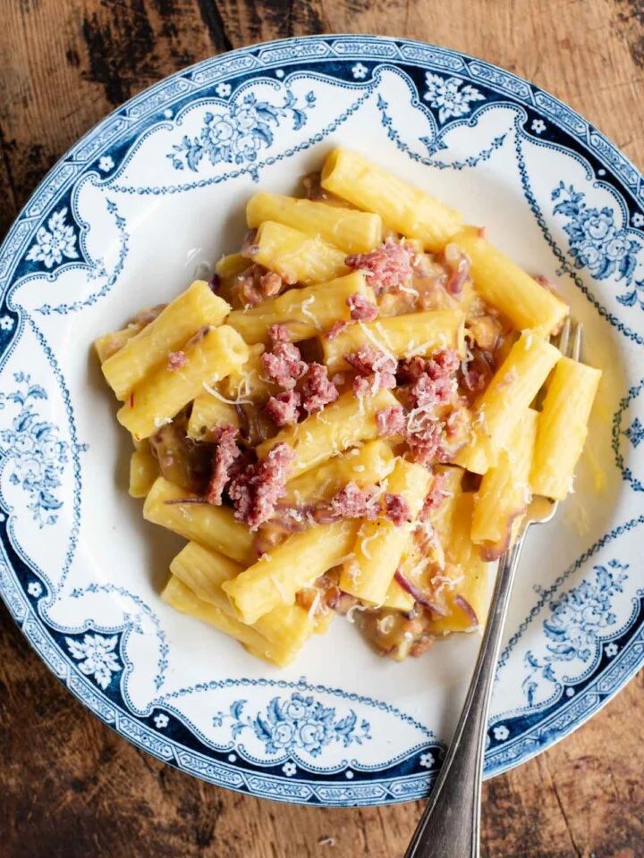 An ovehead shot of a bowl of pasta with potato, saffron and sausage, the background is wooden.
