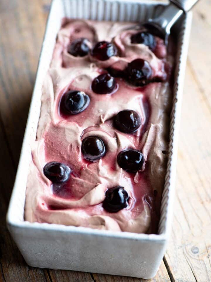 Cherry chocolate ice cream in an ice cream dish with an ice cream scoop at the side.