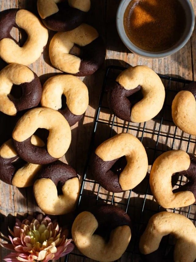 An overhead shot of Italian abbracci cookies (chocolate and cream) on a rustic wooden surface with an espresso at the side.