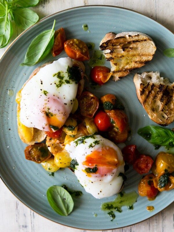 An overhead shot of sauted tomato breakfast crostini topped with poached eggs on a plate