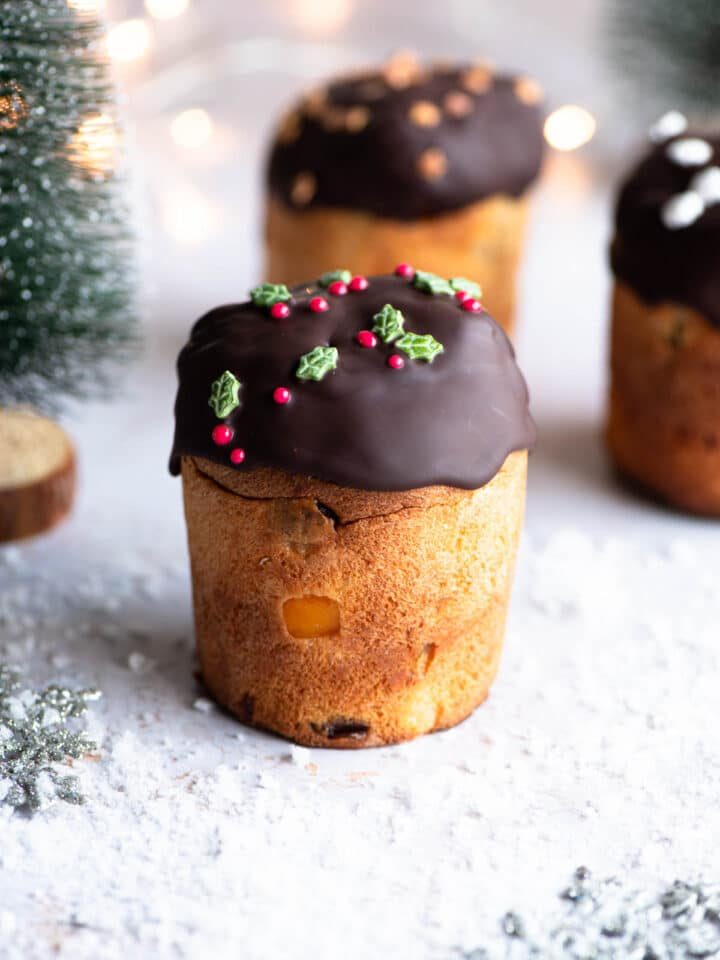 A mini Panettone dipped in melted chocolate sitting on a snowy Christmas themed surface with Christmas trees at the side.