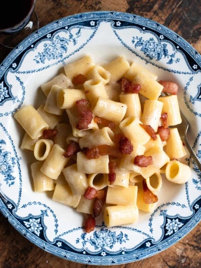 Pasta alla Gricia in a white and blue vintage style bowl sitting on a wooden surface.