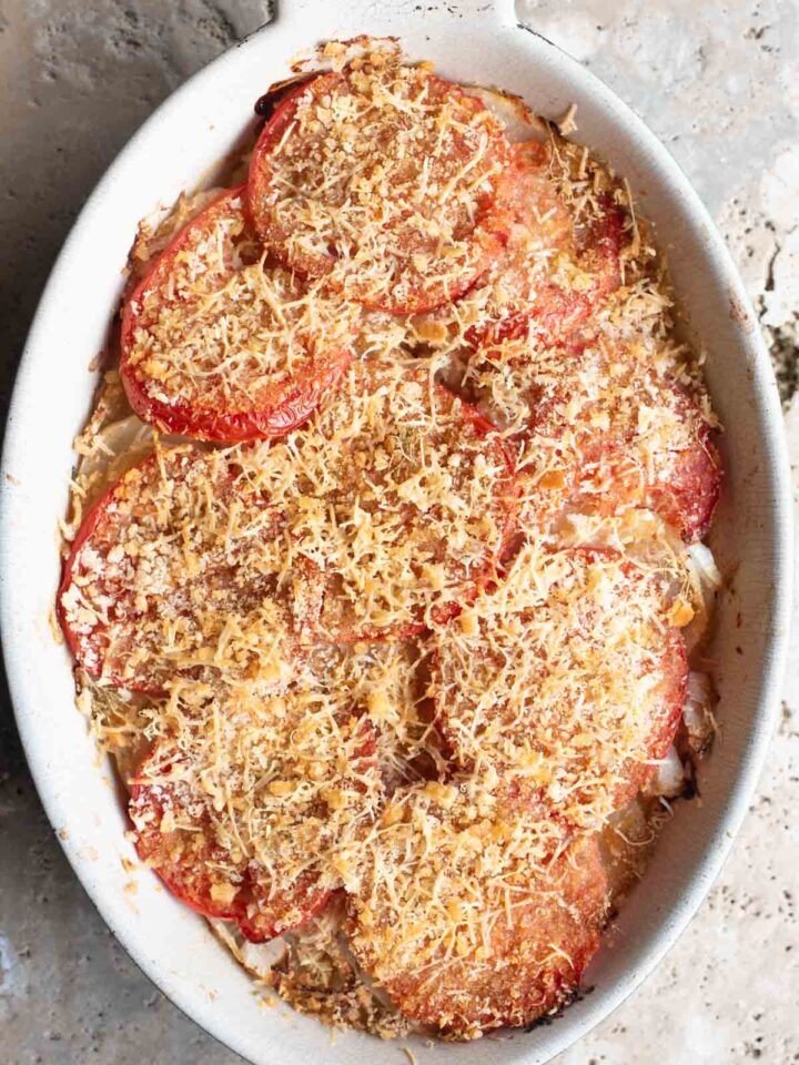 An overhead shot of an Italian potato and tomato gratin in an oval dish sitting on a Travertine background.
