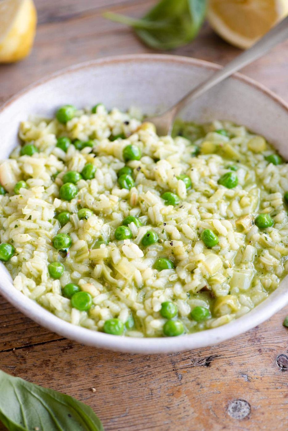 A side shot of a pea and pesto risotto in a bowl in a wooden surface with a fork at the side