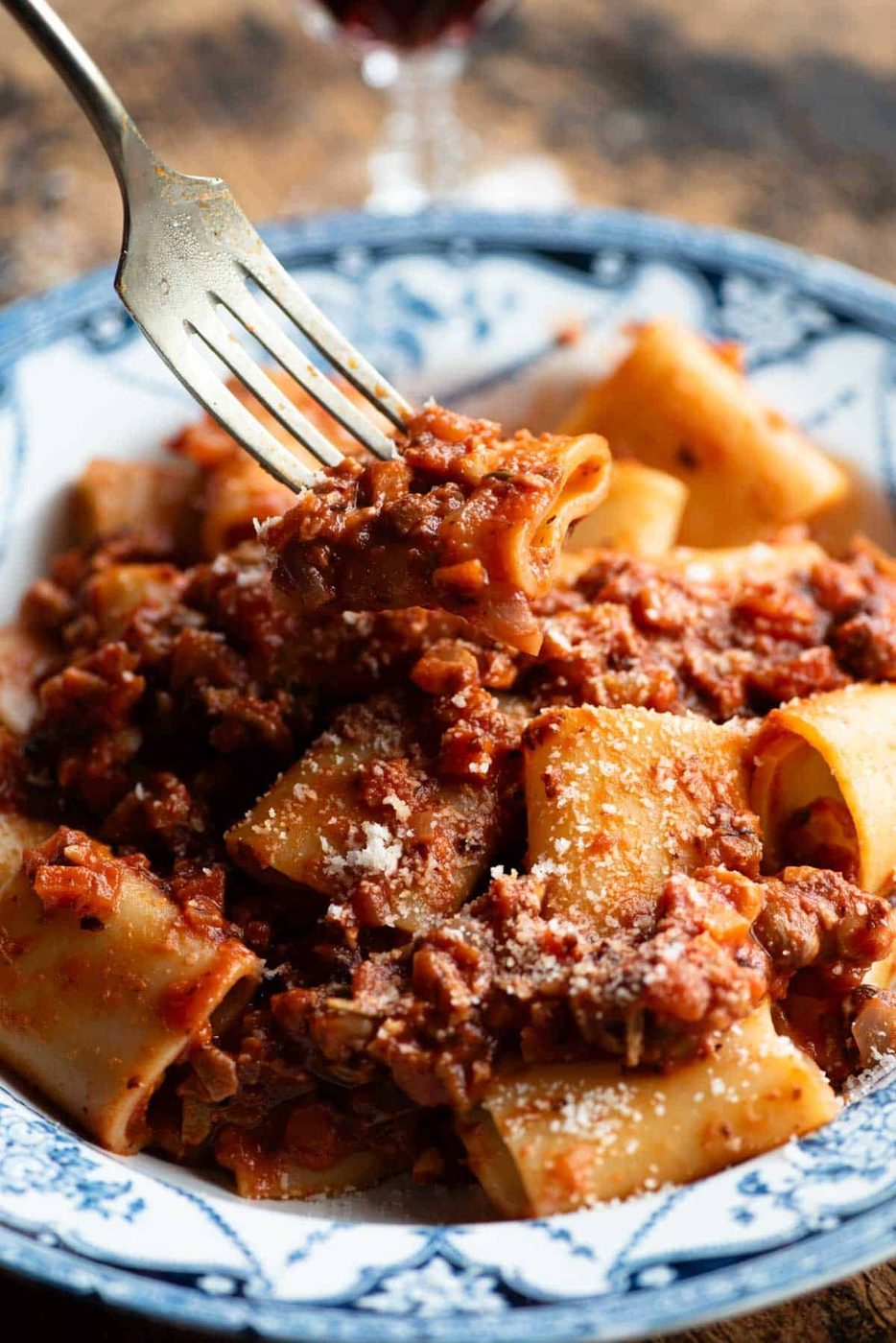 A close up of a fork holding a piece of pasta with hazelnut ragu over a bowl.