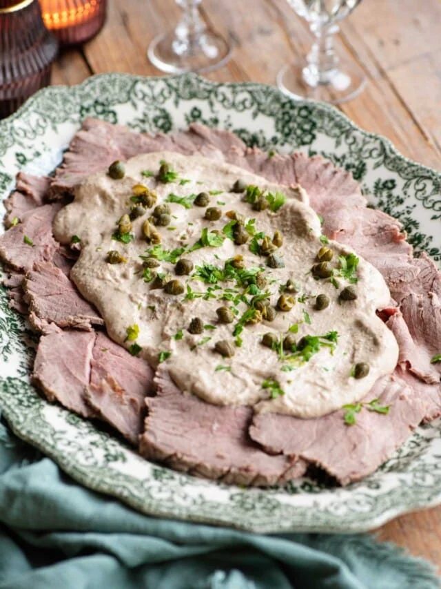 Vitello Tonnato on a serving platter topped with sauce, capers and parsley.