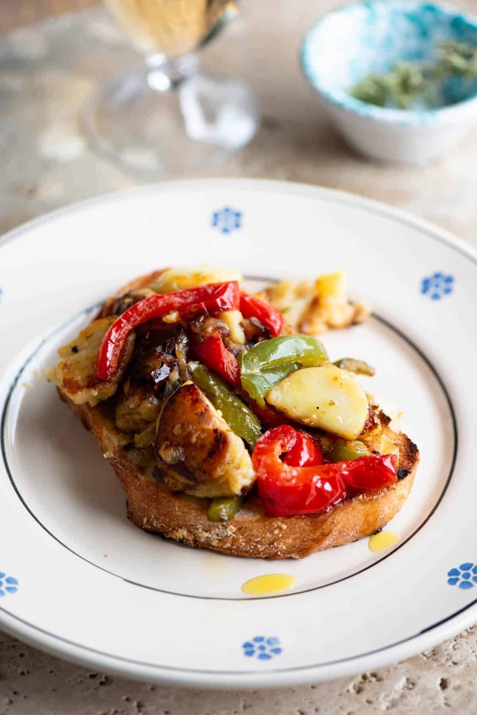 A side shot of peppers and potatoes on a slice of crusty bread sitting on a plate.