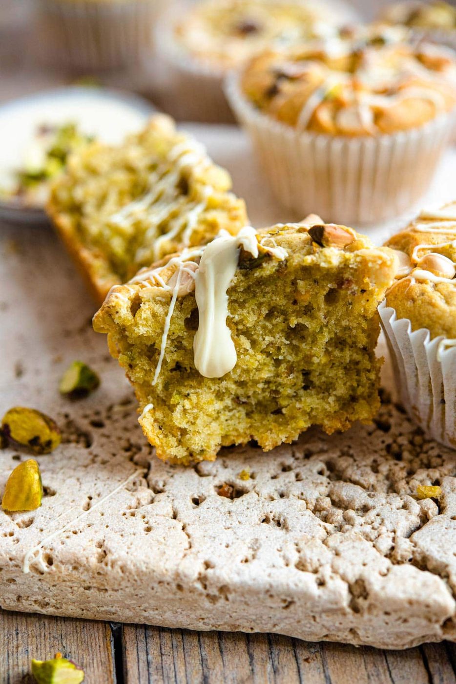 A close up of a pistachio muffin cut in half with white chocolate drizzled on top