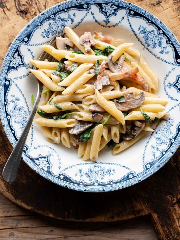 An overhead shot of mushroom spinach pasta in a blue and white bowl.