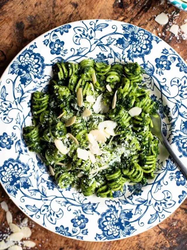 An overhead shot of pasta with kale pesto in a blue floral bowl on a rustic wooden surface.