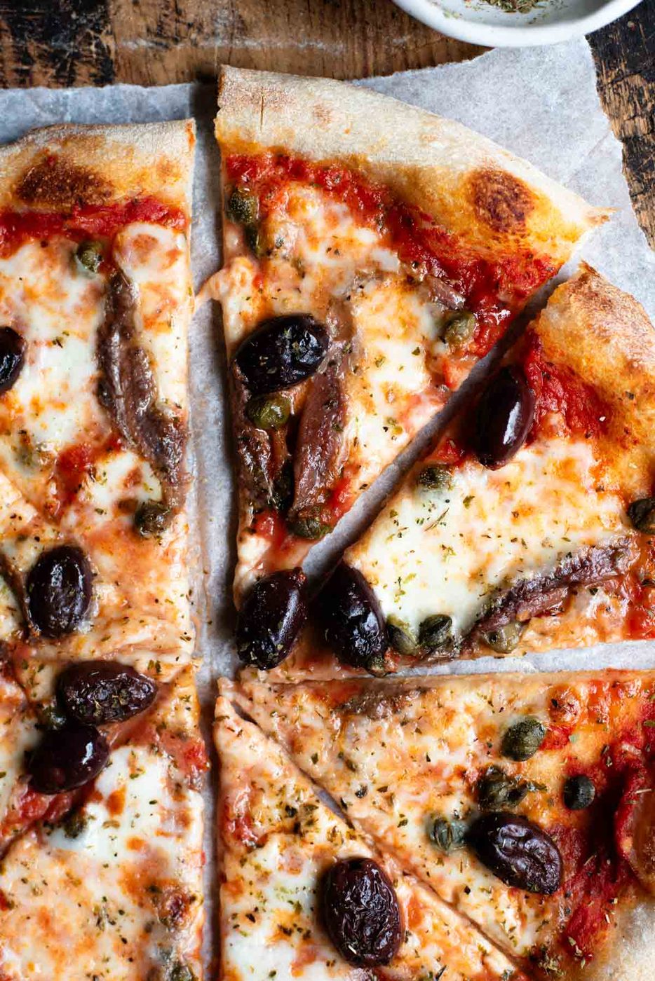 A close up of slices of pizza with mozzarella, tomato, olives, capers and anchovies.