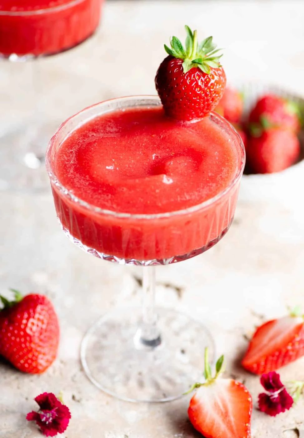 A close up of a frozen strawberry cocktail in a cocktail glass garnished with a strawberry.