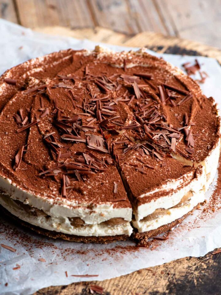 A whole tiramisu cheesecake sitting on a wooden board and parchment paper.