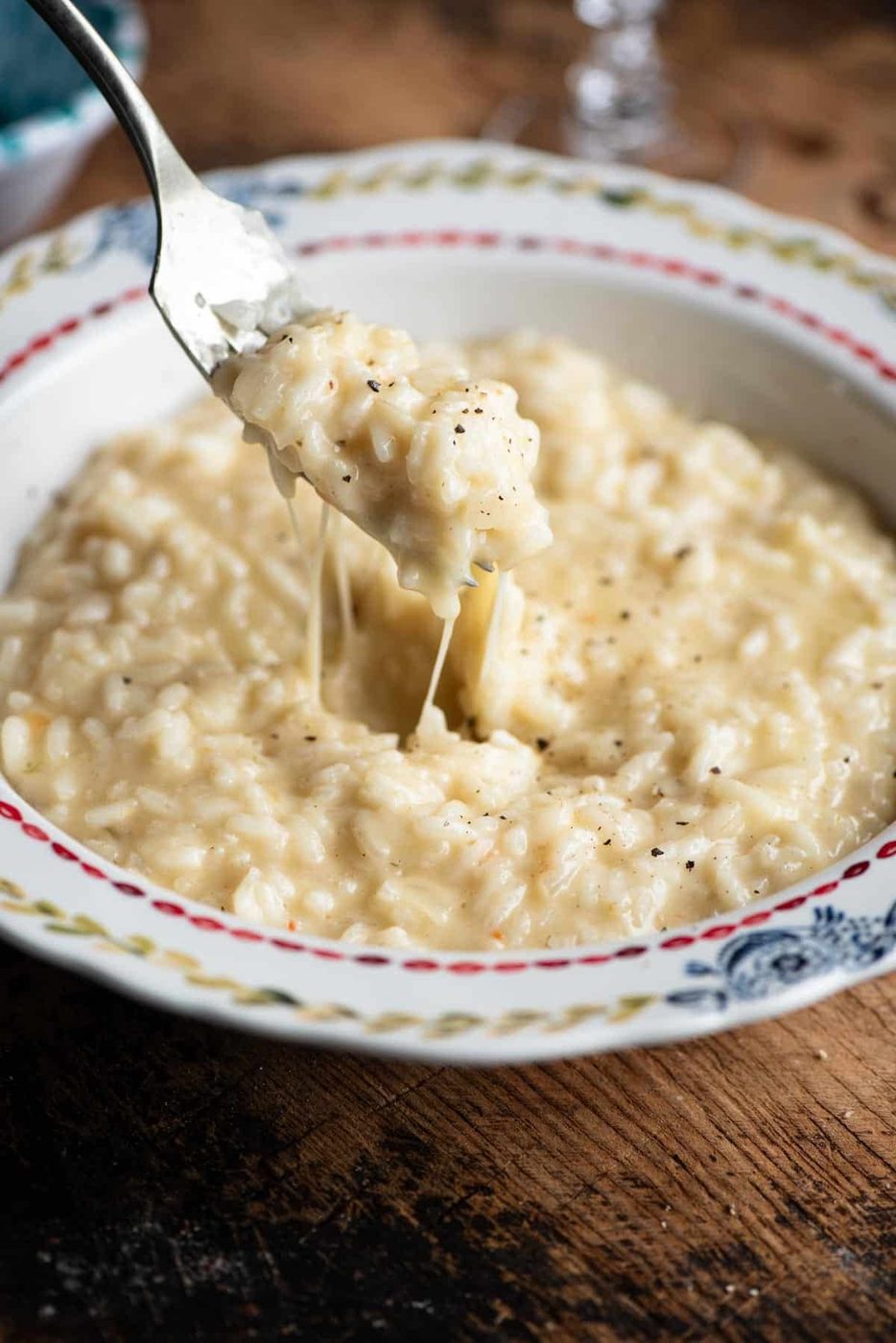 A close up of a fork picking up cheesy risotto from a bowl.