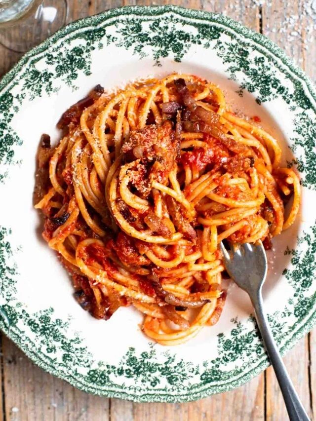 An overhead shot of spaghetti in a green and white vintage style bowl with a tomato and pancetta sauce. The background in rustic wood.