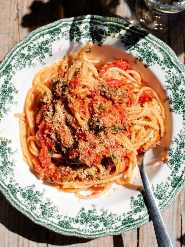 An overhead shot of spaghetti in a tomato sauce with sardines and breadcrumbs on top. The bowl is a vintage style green and white colour.