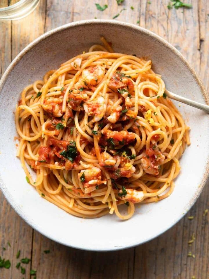 An overhead shot of shrimp spaghetti in a rustic bowl sitting on a wooden surface with a glass of white wine at the side.