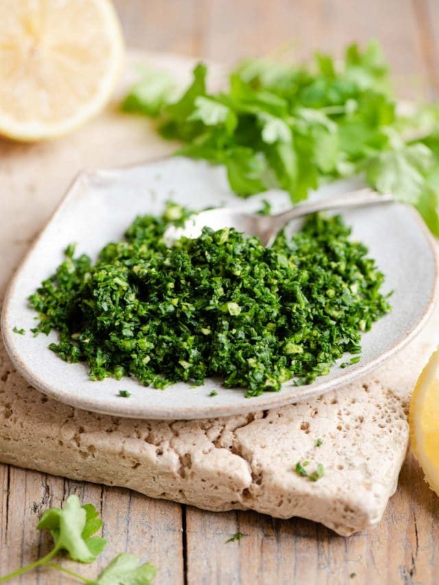 Gremolata on a small plate with wedges of lemon and parsley in the background
