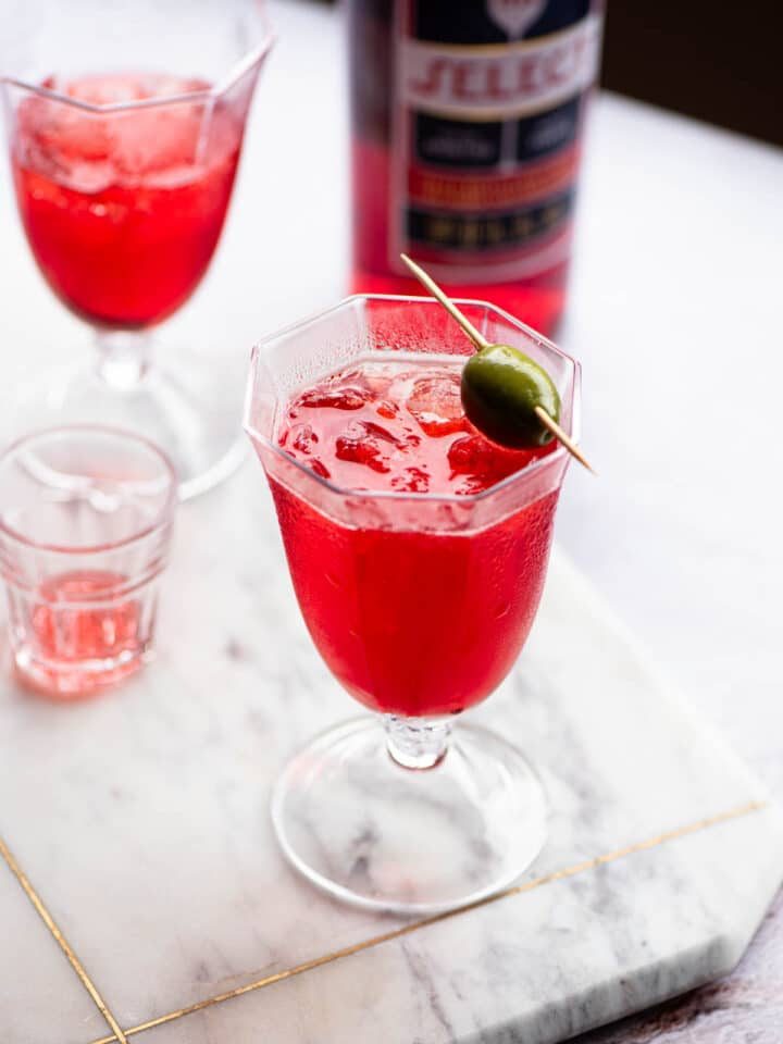 A select spritz in a glass topped with an olive.