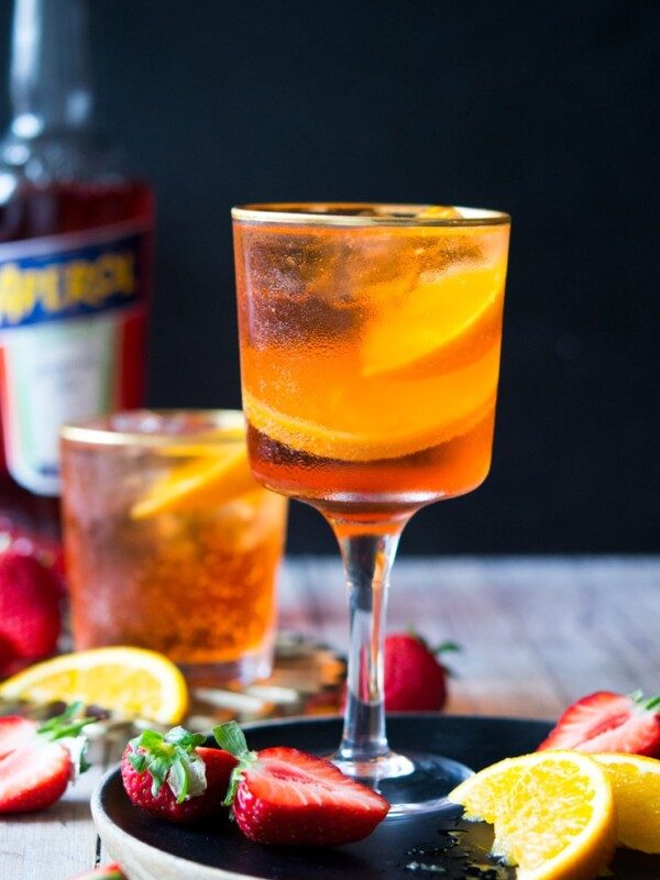 An aperol spritz cocktail in a wine glass with strawberries and oranges