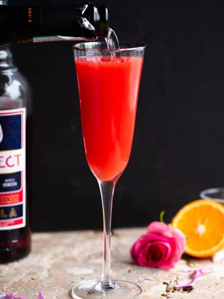 A select mimosa in a flute glass with prosecco getting poured in.