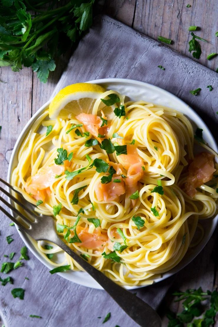 a close up of smoked salmon pasta on a plate and sitting on a wooden surface