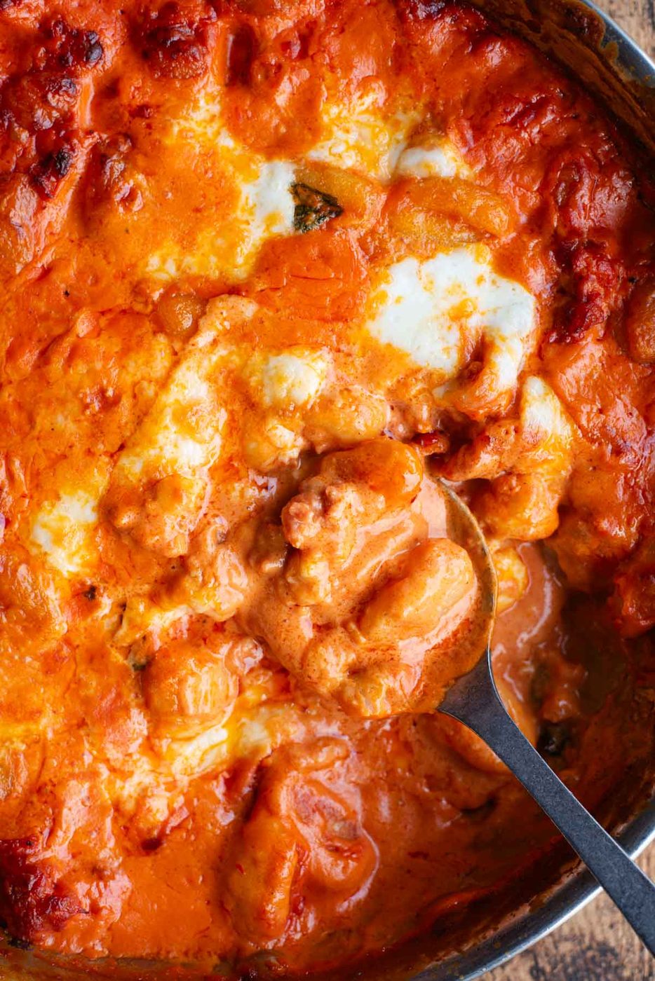 A close up of creamy baked gnocchi in a pan with a serving spoon.