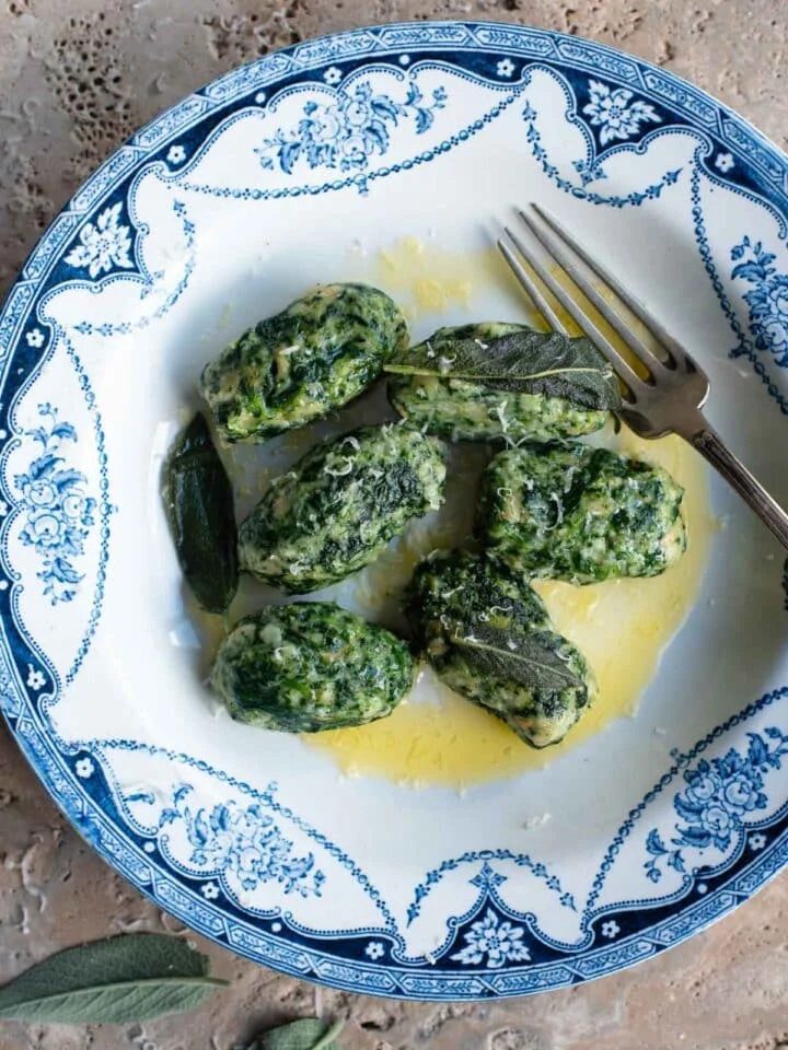 An overhead shot of Strangolapreti (Italian bread dumplings) on a blue and white plate sitting on a stone work surface.