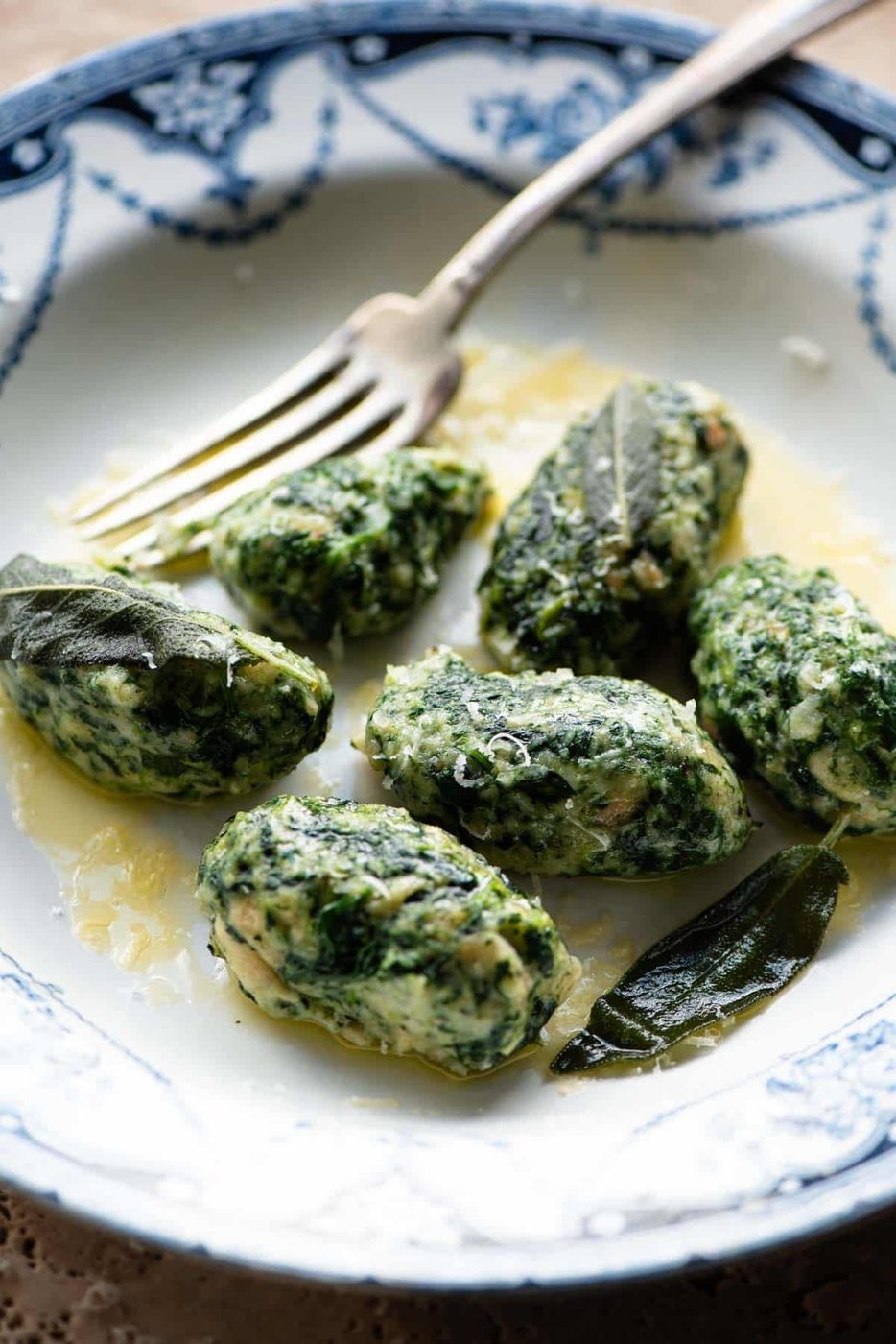 A side shot of Strangolapreti (italian bread dumplings) on a plate with butter and sage.