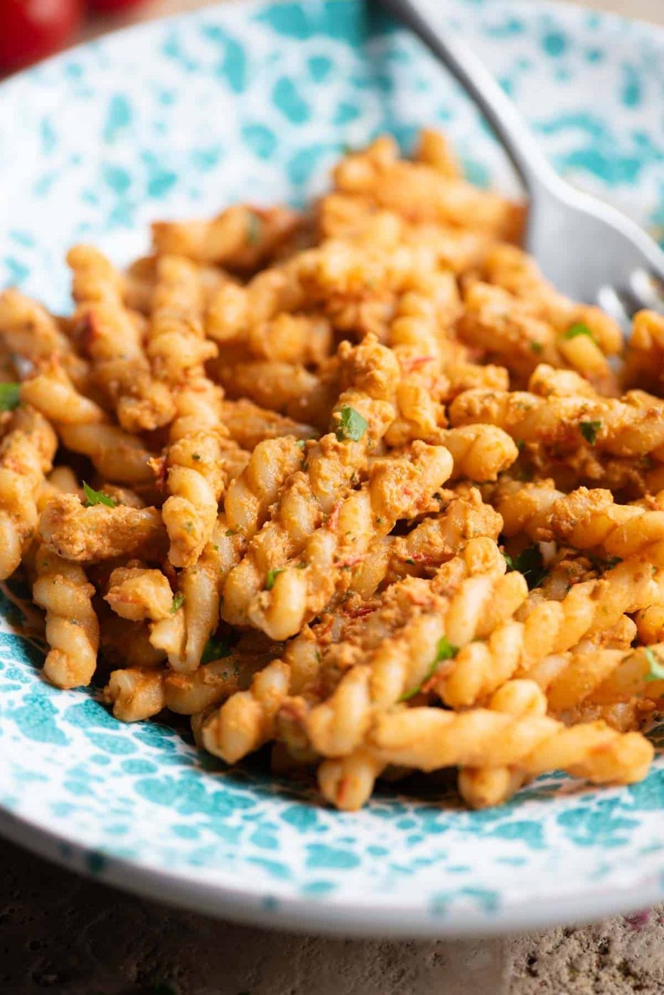 A close up of fusilli pasta with a tuna and tomato sauce in a blue and white bowl.