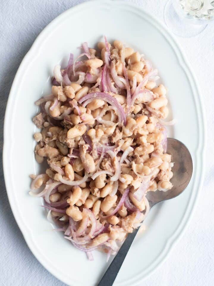 An overhead shot of cannellini beans, tuna and onion on a white platter.