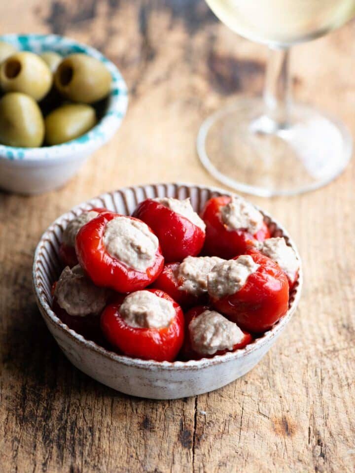 Tuna stuffed cherry peppers in a small dish with olives and a glass of wine at the side.