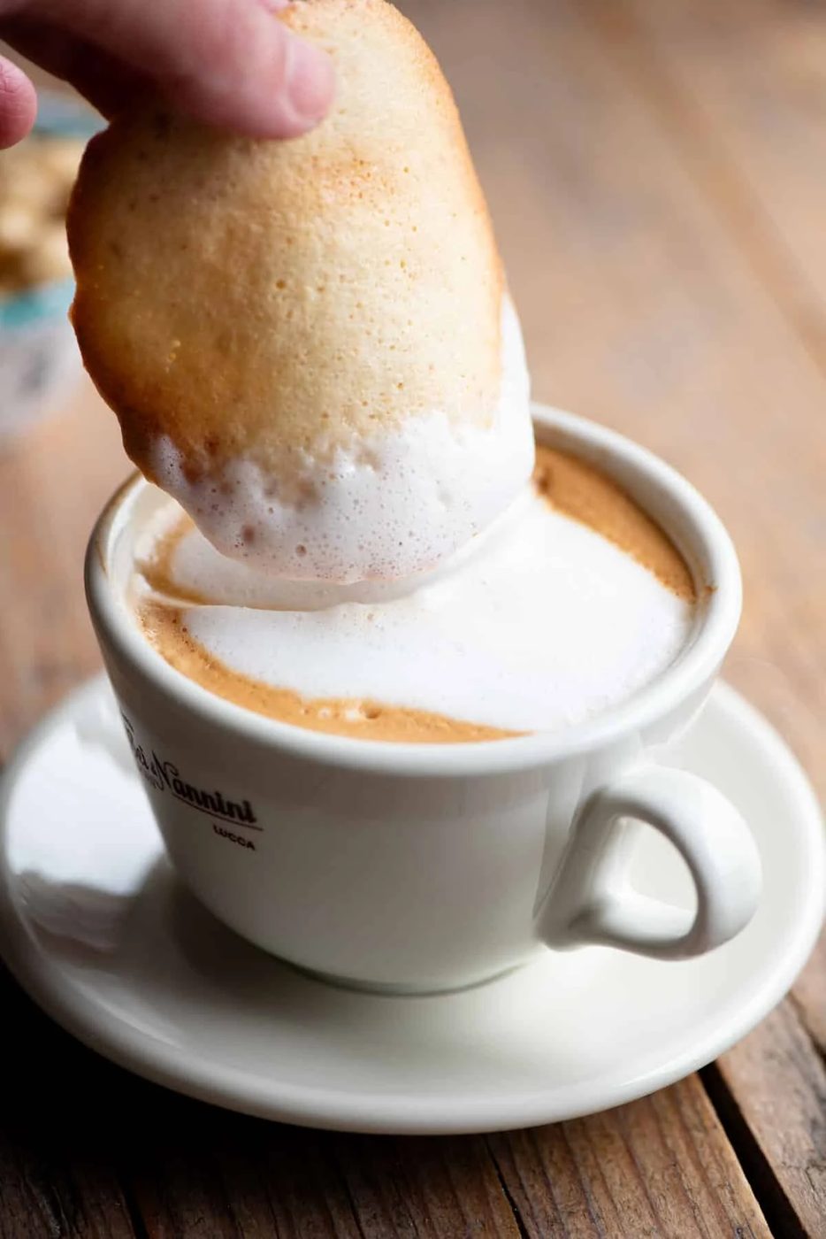 A close up of an Italian cookie called Tegola Valdostana getting dunked into a cappuccino.