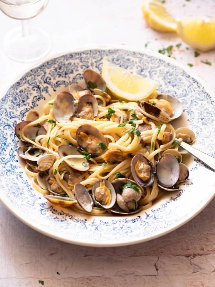 Linguine alle Vongole in a blue bowl with a slice of lemon at the side.