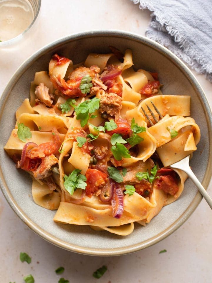 An overhead shot of tuna pasta in a bowl with tomatoes, capers and parsley