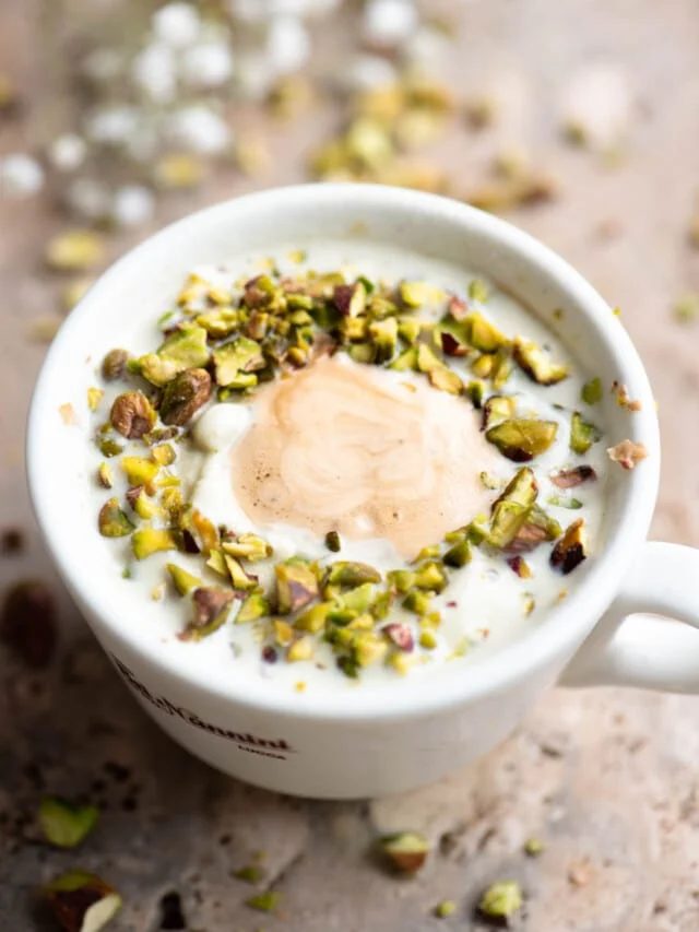 A pistachio affogato topped with chopped pistachios on a travertine surface.