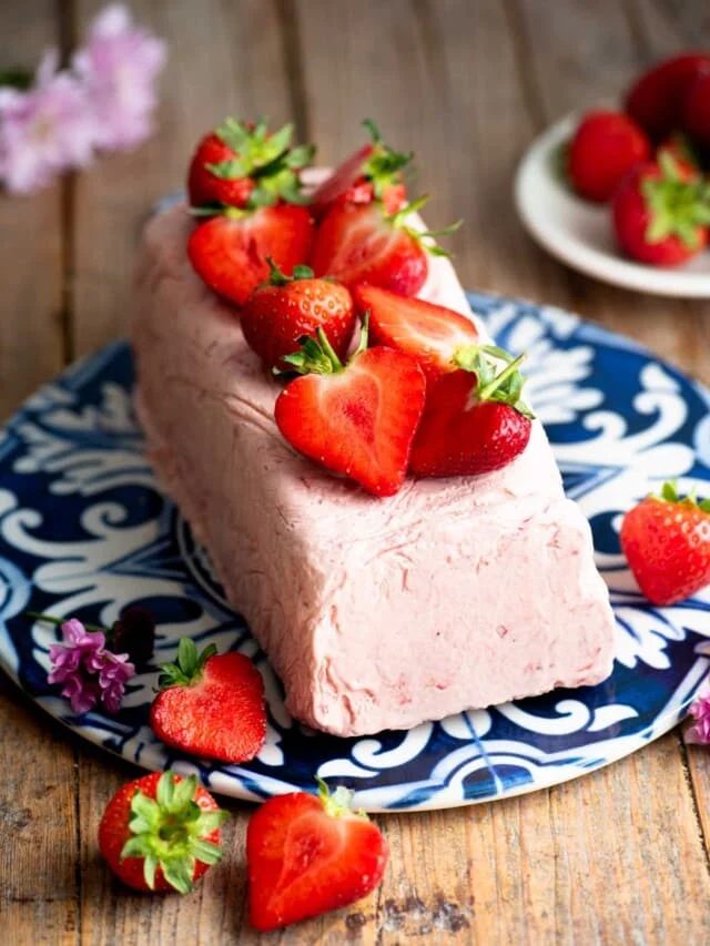 Strawberry semifreddo on a blue and white ceramic serving board topped with cut strawberries.