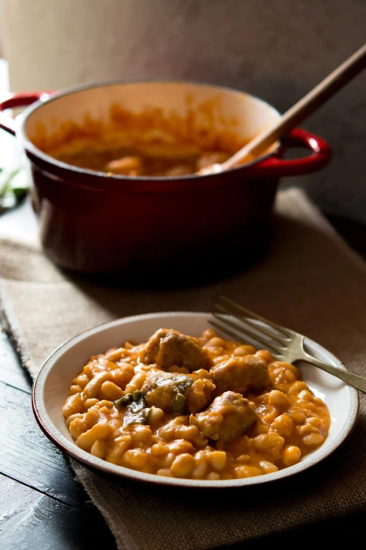 A close up of Tuscan Bean Stew, plus Sausages on a plate with a fork, pot in the background.