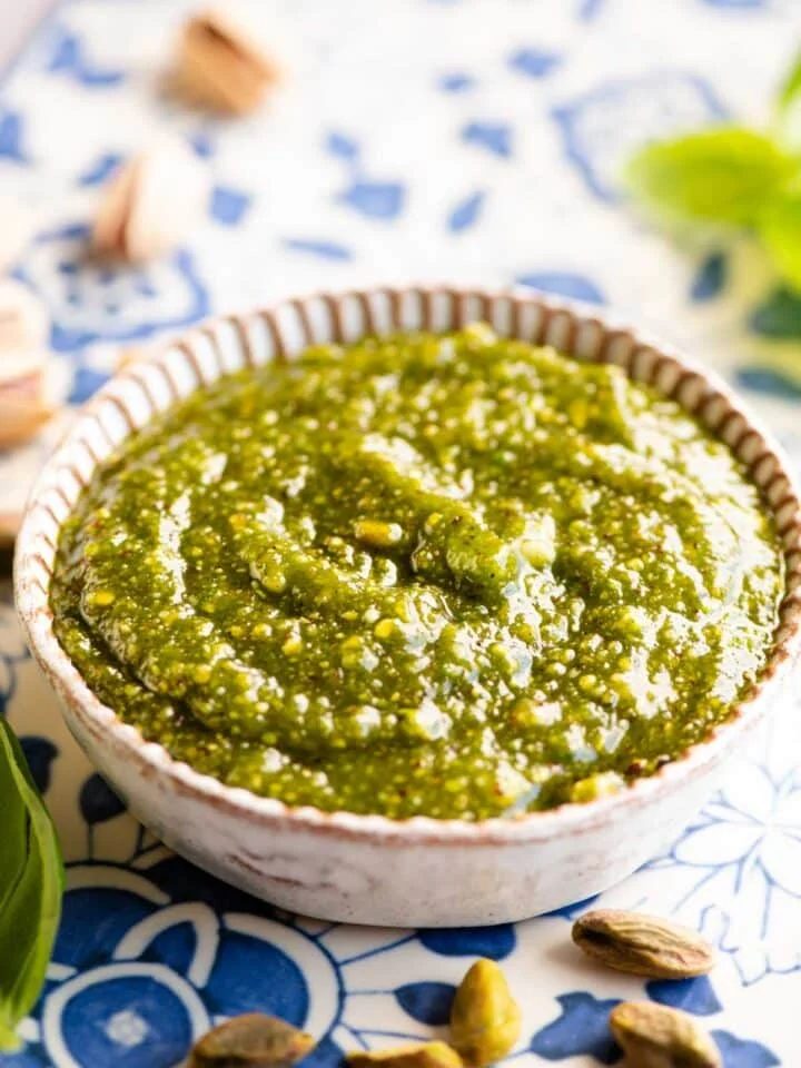 Pistachio pesto in a small round dish sitting on a blue patterned board.