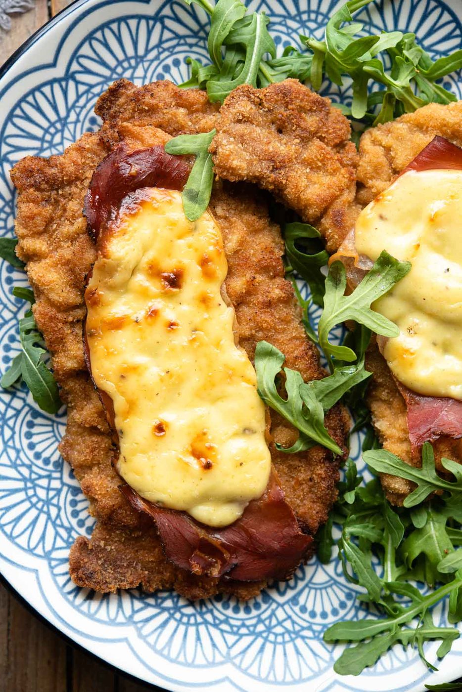 An overhead shot of breaded veal cutlets on a plate topped with parmesan cream and prosciutto