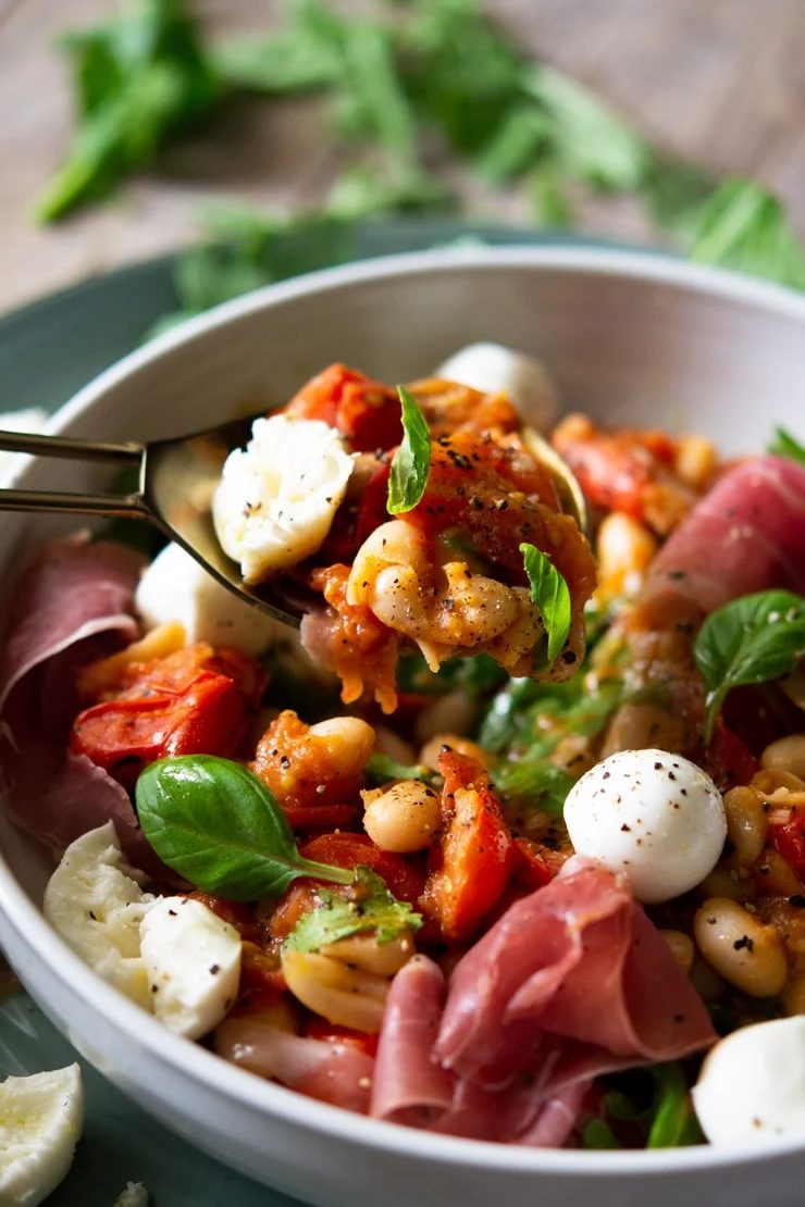 A close up of a white bean salad with tomato on a serving spoon