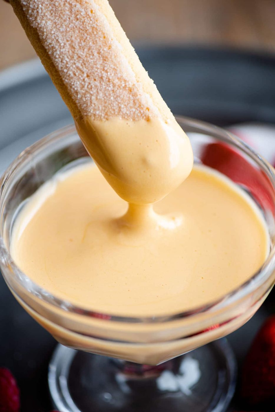 A close up of a savoiardi cookie being dunked into zabaglione