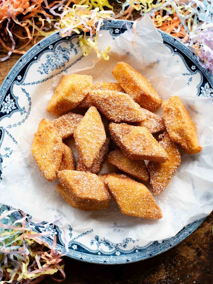 An overhead shot of Crema Fritta (fried custard bites) in a bowl topped with powdered sugar. There's confetti sprinkled around.