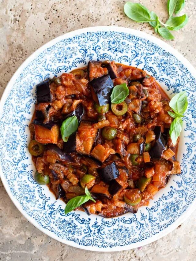 Sicilian caponata in a blue patterned bowl sitting on a travertine surface.