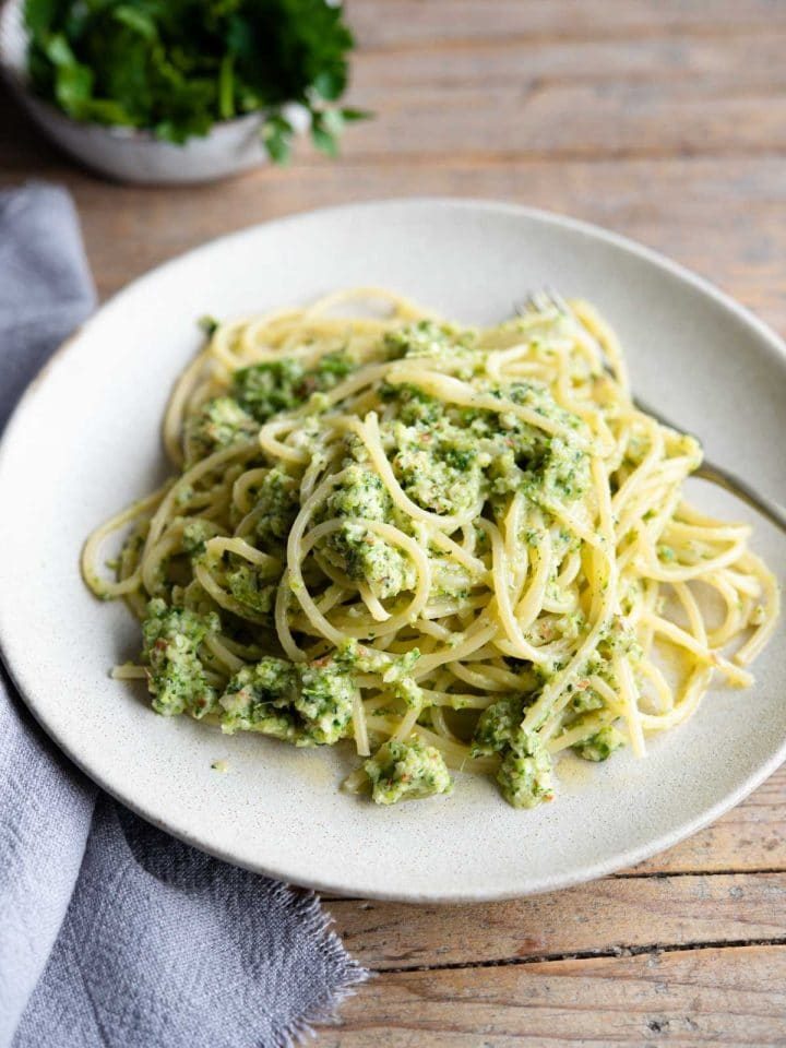 A plate for zucchini pesto pasta on a wooden surface with a blue towel at the side