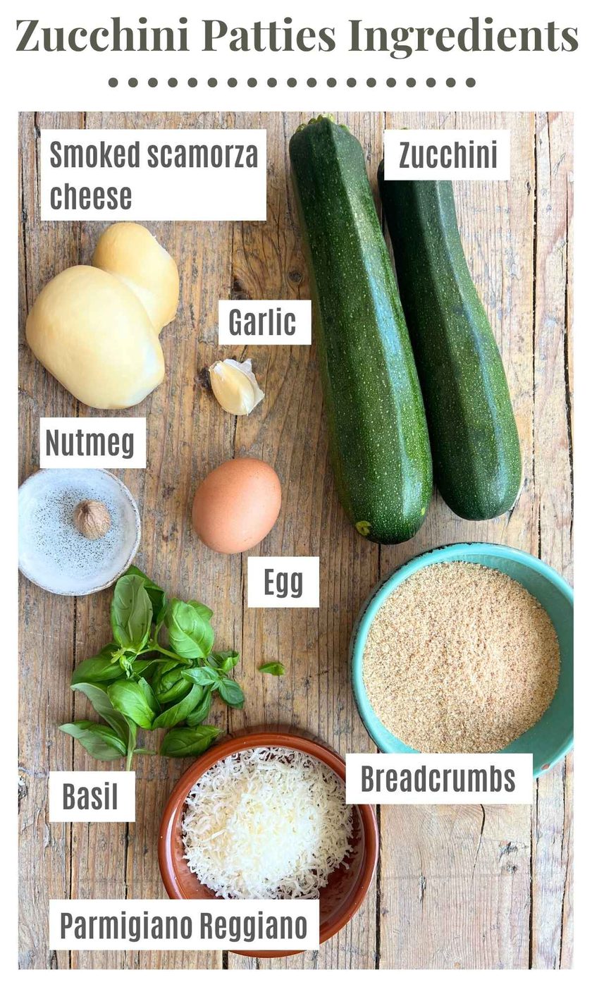 All the ingredients needed to make cheesy zucchini patties on a wooden board.Ingredient labels next to each ingredient read; zucchini, smoked scamorza cheese, egg, garlic, breadcrumbs, nutmeg, basil, parmigiano reggiano.