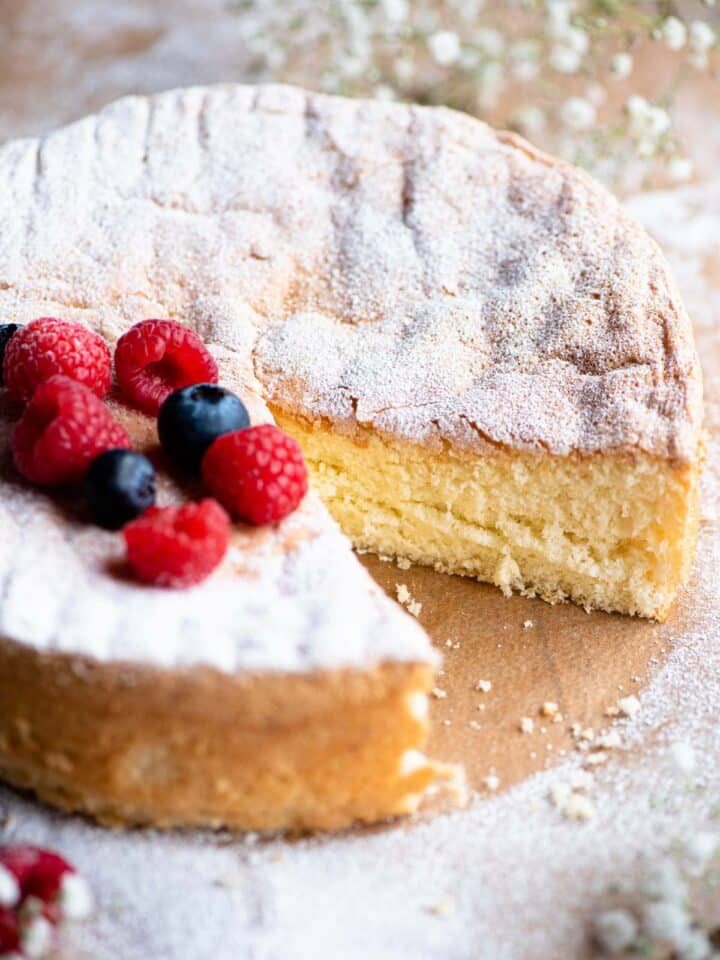 A close up of an Italian Pan di Spagna sponge cake with a slice cut out and berries on the top.