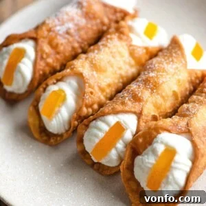 A close up of four homemade cannoli filled with ricotta and topped with candied orange on a plate